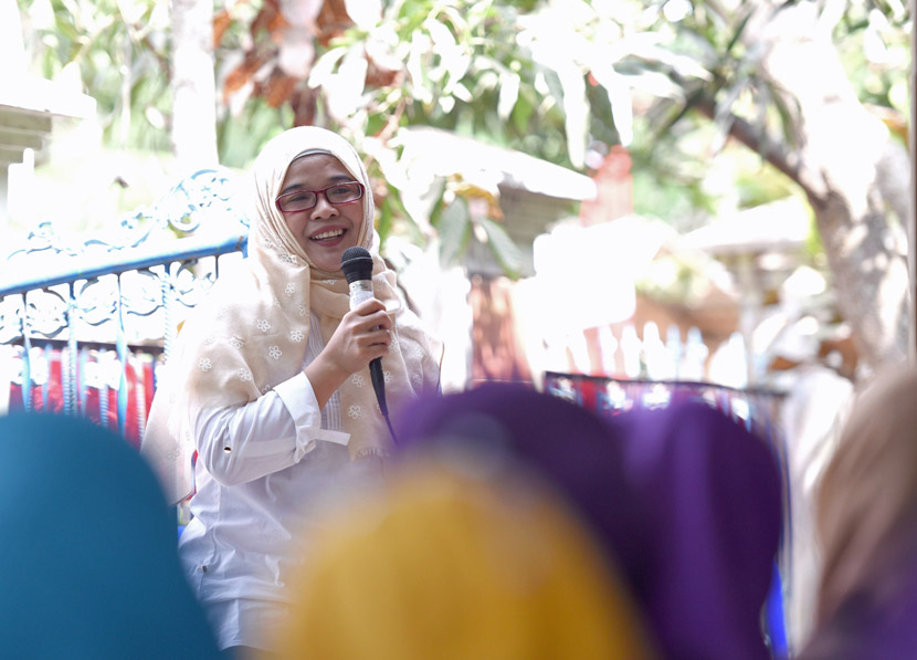 A woman with hijab and red glasses is talking holding a microphone to a group of women